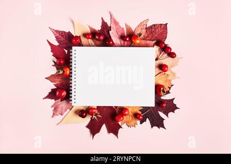 Cahier avec cadre de feuilles colorées d'automne et de baies sur fond rose. Concept créatif Hello Autumn Banque D'Images