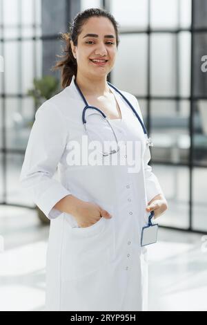 Femme dentiste debout avec les bras croisés. Dentiste confiant debout dans un couloir d'hôpital dans un manteau blanc. Banque D'Images