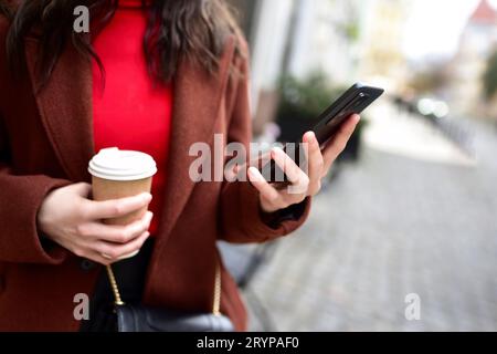 Les mains de la femme recadrée tenant le téléphone intelligent avec une tasse de café. Banque D'Images