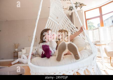 Deux petites filles montent sur une balançoire macramé à la maison près du sapin de Noël. Les sœurs s'amusent, se trompent en vacances. Amies drôles ayant un hap Banque D'Images