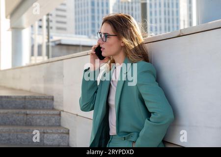 Femme d'affaires debout sur les escaliers à l'extérieur de l'immeuble de bureaux tout en parlant sur le téléphone portable Banque D'Images