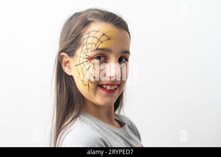 Belle fille adolescente aux yeux bruns, cheveux longs, sourire et regarder vers le bas dans un chapeau vert avec araignées noires et toile pour la fête de costume, avec maquillage d'eau Banque D'Images