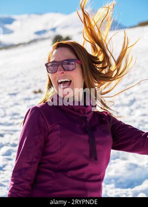 Femme d'âge moyen ayant un grand temps sur une journée ensoleillée dans la neige tout en jouant avec ses cheveux, concept de personnes sans complexes et style de vie. Verti Banque D'Images