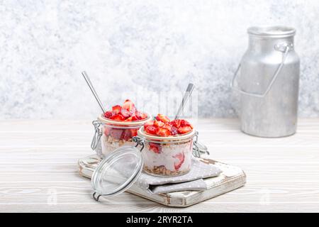 Parfait avec des fraises, yaourt et granola en verre transparent Mason jarres sur fond blanc rustique en bois angle View et Banque D'Images