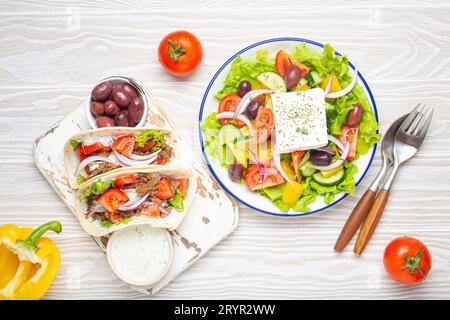 Cuisine grecque traditionnelle : salade grecque, Gyros avec viande et légumes, sauce Tzatziki, olives sur table blanche rustique en bois backgro Banque D'Images