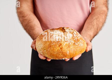 Boulanger en tablier tenant une miche de pain frais dans les mains Banque D'Images