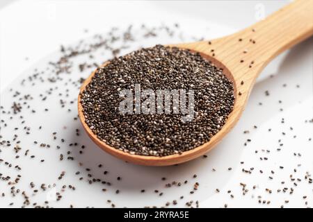 Cuillère en bois de graines de chia saines. Source d'acides gras Oméga 3 sur la surface de céramique blanche en gros plan Banque D'Images