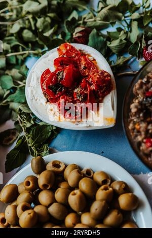 Une exposition vibrante de cuisine méditerranéenne avec tomates, olives, fromage et pain sur une table bleue rustique Banque D'Images