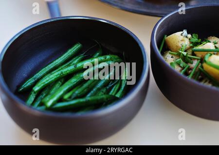 Un bol en céramique sombre de haricots verts, un bol de petites pommes de terre, des plats d'accompagnement du menu du déjeuner - cuisine fine au Bennelong Restaurant, Sydney, Australie Banque D'Images