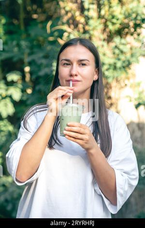 Femme élégante buvant du matcha latte dans le parc. Banque D'Images