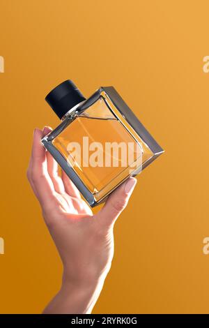 Flacon de parfum dans les mains sur un fond orange. Banque D'Images