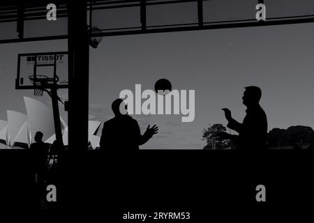Des hommes en silhouette jetant un ballon de basket-ball Sydney Opera House vus « encadrés » depuis la salle de fret OSPT et un panier de basket-ball américain Banque D'Images
