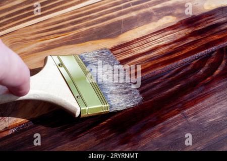 Les planches de bois sont à moitié recouvertes de teinture. Une brosse avec un manche en bois et des poils naturels sur un fond de planches de bois peintes. Le tableau pr Banque D'Images