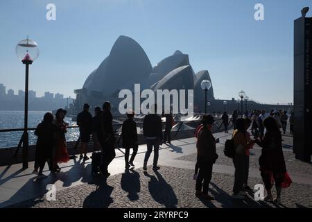 Petits groupes de touristes arrivant à la vue complète de l'Opéra de Sydney sur Bennelong point, un matin brumeux avec un port bleu étincelant Banque D'Images