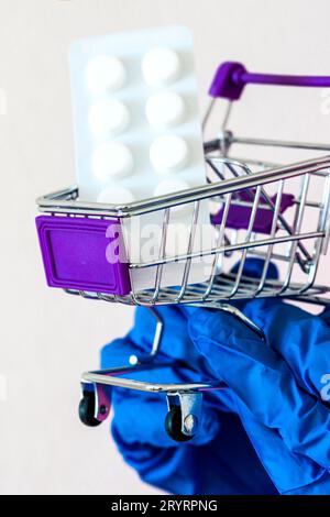 Chariot de magasin, pilules. les mains dans les gants tiennent un chariot avec des médicaments. matériel médical. Concept de pénurie de fournitures médicales. Demande conceptuelle, ventes Banque D'Images