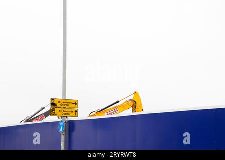 Nouveau développement à St. Leonards Exeter - signalisation jaune pour St. Leonards quart de ventes, avec élévateur jaune assorti derrière un mur de barrière bleu Banque D'Images