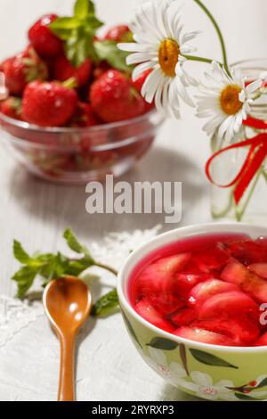 Gelée de cerises avec des morceaux de fraises dans le bol et des fleurs Banque D'Images