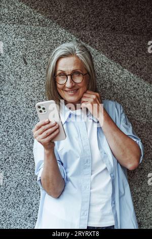 Concept de communication dans la vieillesse, femme âgée mature utilisant le téléphone mobile pour les SMS et les messagers Internet. La femme est active Banque D'Images
