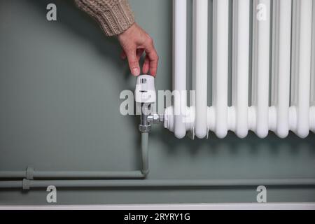 Gros plan de la main baisser le thermostat sur le radiateur à la maison pour économiser de l'énergie et de l'argent Banque D'Images