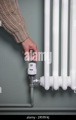 Gros plan de la main baisser le thermostat sur le radiateur à la maison pour économiser de l'énergie et de l'argent Banque D'Images
