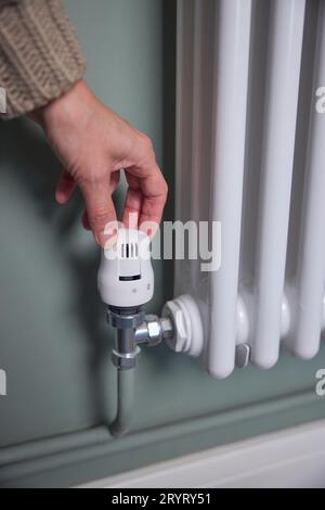 Gros plan de la main baisser le thermostat sur le radiateur à la maison pour économiser de l'énergie et de l'argent Banque D'Images
