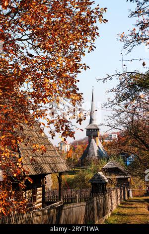 Eglise en bois dans la distance et entre les arbres colorés d'automne dans le parc ethnographique Romulus Vuia Banque D'Images