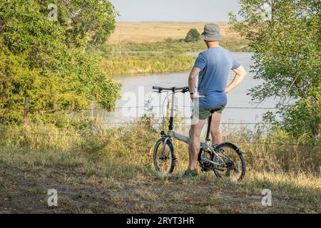 Un homme âgé athlétique regarde Dismal River après avoir monté un vélo pliant dans Whitetail Campground dans la forêt nationale du Nebraska Banque D'Images