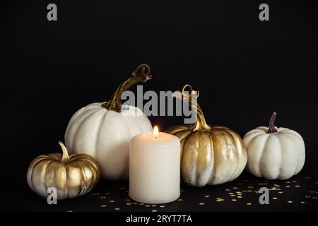 Composition Halloween avec citrouilles dorées et bougie allumée sur fond noir Banque D'Images