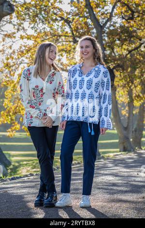 Deux jeunes femmes, amies, partagent la conversation sous les imposants arbres d'automne, rétroéclairés par le soleil de l'après-midi Banque D'Images