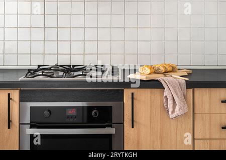 Baguette en tranches repose sur une planche de bois sur une table à côté de la cuisinière à gaz sur fond de carreaux blancs dans une chambre d'hôtel cinq étoiles de luxe. Concept de voyage Banque D'Images