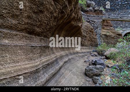 Cette image montre un chemin de terre sinueux et bosselé menant à un pont étroit dans un paysage montagneux Banque D'Images