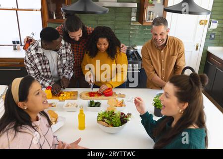 Heureux divers amis masculins et féminins préparant le repas et buvant des boissons dans la cuisine Banque D'Images