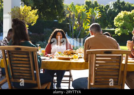 Heureux divers amis masculins et féminins priant avant le repas de célébration de Thanksgiving dans le jardin ensoleillé Banque D'Images