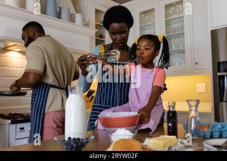 Mère afro-américaine et fille mélangeant la pâte avec fouet dans un bol sur la table dans la cuisine Banque D'Images