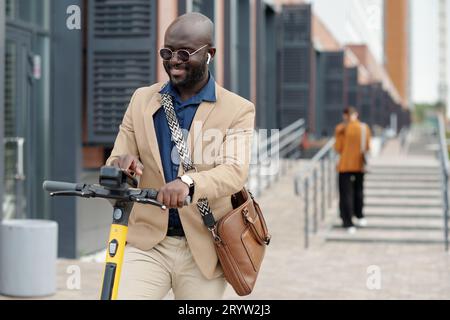 Jeune souriant homme solopreneur dans formalwear choisissant des paramètres de scooter contre employé féminin avant de monter à la maison après le travail Banque D'Images