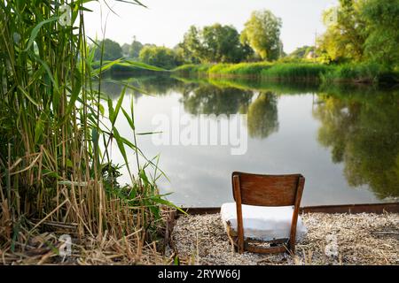Une chaise maison se dresse sur la rive du lac parmi les roseaux avec le lac en arrière-plan. Hobby, pêche pour l'âme. Belle vue sur le lac Banque D'Images