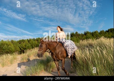 Une femelle chevauchant un cheval dans un champ vert par un jour de bleu Banque D'Images