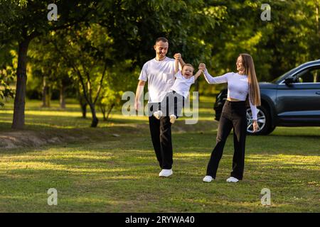Famille passant du temps ensemble en vacances. Mère, père vomit enfant et courir dans la rue près de la forêt dans la nature. Banque D'Images