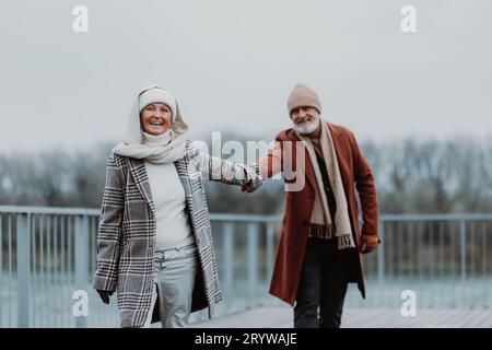 Élégant couple senior marchant près de la rivière, pendant la journée froide d'hiver. Banque D'Images