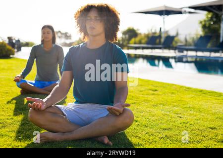 Groupe d'amis divers faisant du yoga et méditant dans le jardin Banque D'Images