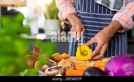 Section médiane de l'homme biracial portant un tablier préparant le repas, coupant les légumes dans la cuisine, espace de copie Banque D'Images