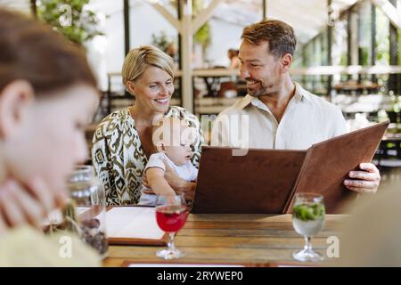 Famille avec des menus de lecture de bébé dans un restaurant, choisir la nourriture et les boissons. Banque D'Images