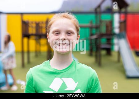 Portrait d'écolière caucasienne souriante portant un t-shirt de recyclage dans la cour d'école, avec espace de copie Banque D'Images