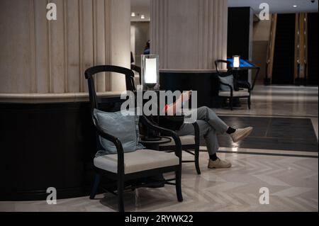 03.08.2023, Singapour, République de Singapour, Asie - Un client de l'hôtel est assis derrière une lampe dans le hall de l'hôtel Shangri-la regardant son téléphone. Banque D'Images