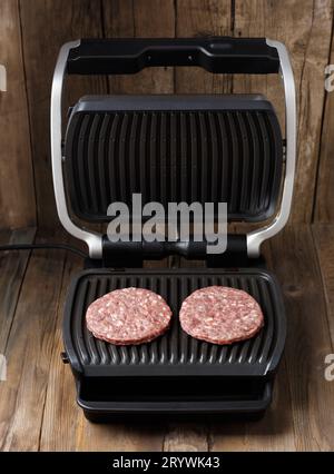 Les galettes de bœuf pour un hamburger sont frites sur un gril électrique intelligent. Cuisson des hamburgers faits maison. Ingrédients pour hamburgers. Banque D'Images