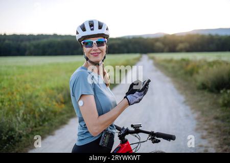 Cycliste diabétique avec moniteur de glycémie en continu vérifiant sur smartphone son taux de sucre dans le sang en temps réel. Banque D'Images