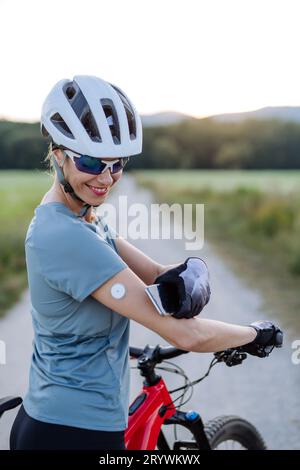 Cycliste diabétique avec moniteur de glycémie en continu vérifiant sur smartphone son taux de sucre dans le sang en temps réel. Banque D'Images