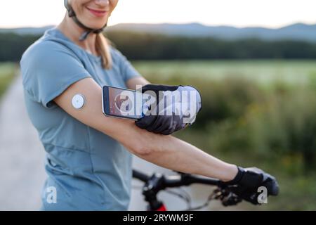 Cycliste diabétique connectant un moniteur de glycémie continu à son smartphone pour surveiller son taux de sucre dans le sang en temps réel. Banque D'Images