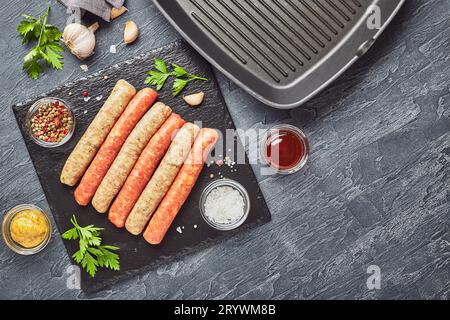 Saucisses de viande crues sur une plaque d'ardoise, avec herbes et épices et une poêle à grillades carrée.Vue de dessus Banque D'Images