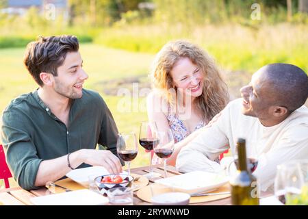 Famille et amis multiethniques se rassemblant à une table de jardin. Gens mangeant des légumes grillés et frais, partage Banque D'Images